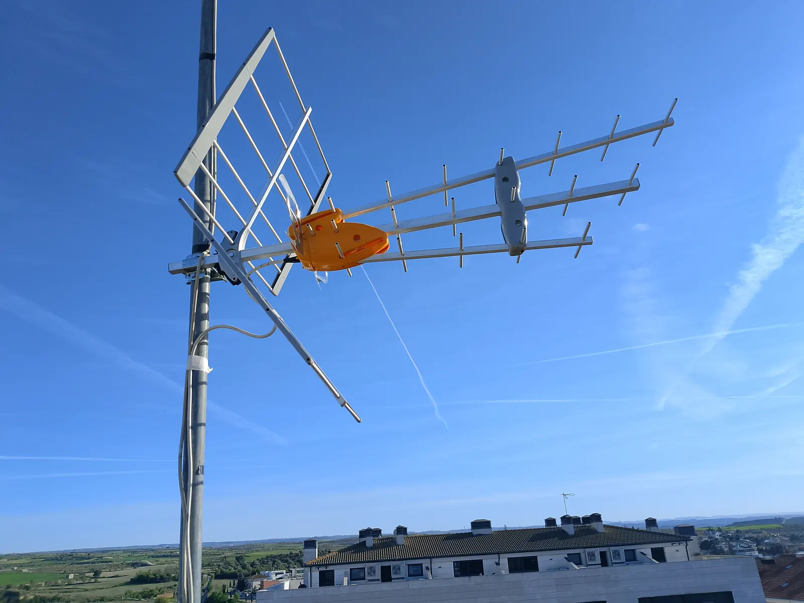 Antena de TDT y parabólica en mástil sobre tejado.