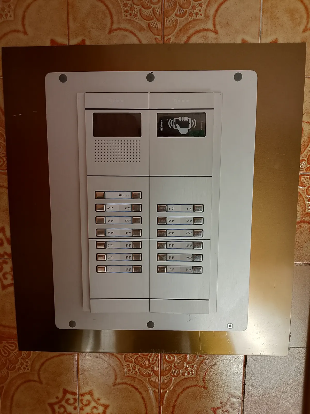 Placa de videoportero con pantalla y botonera en una comunidad de vecinos.